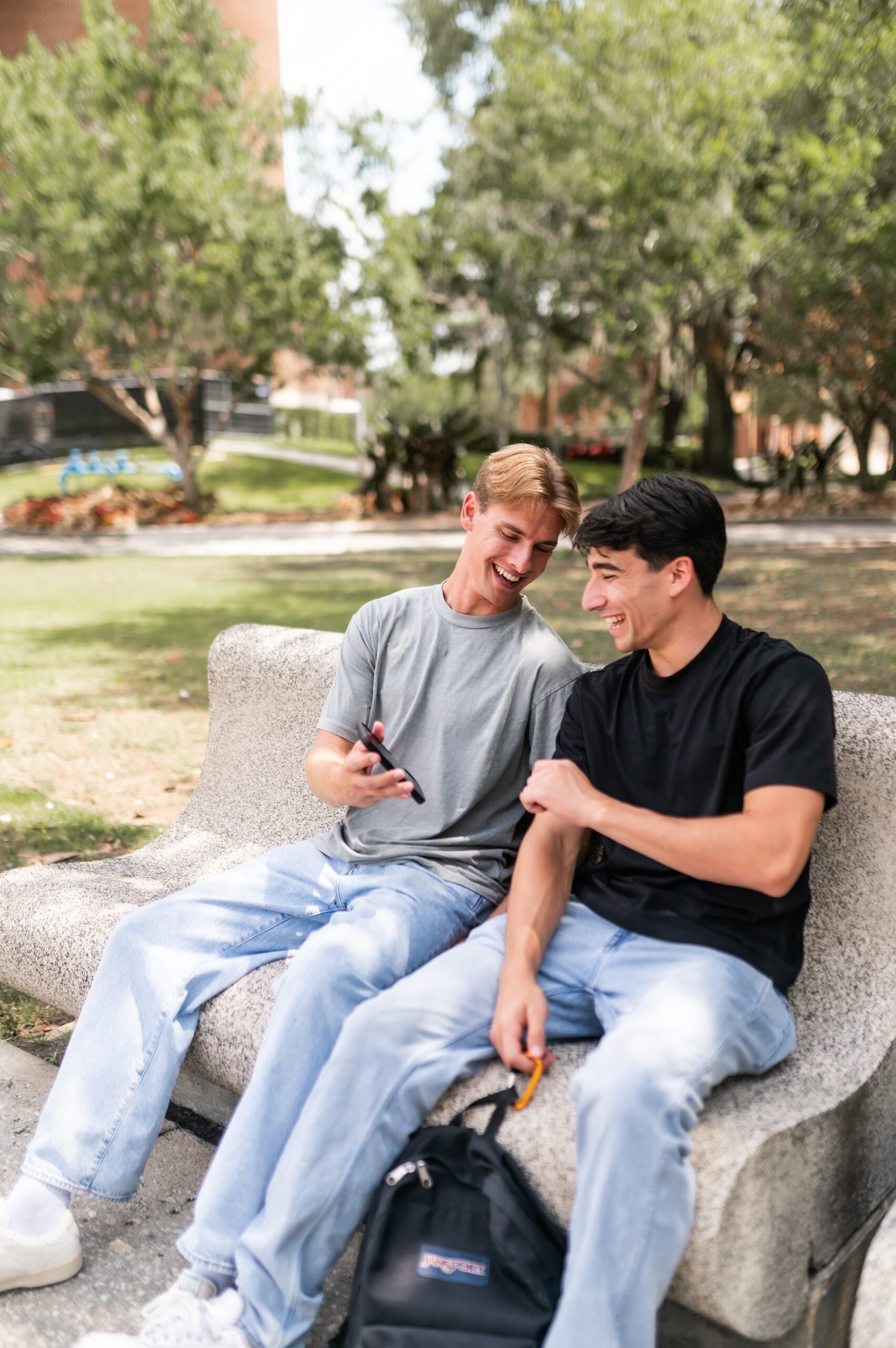 Friends laughing at smartphone on bench