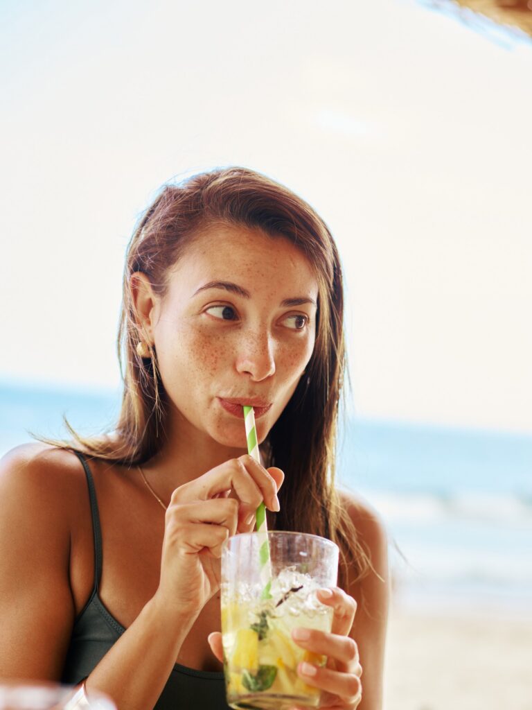 Young woman sipping a fresh fruit drink by the water
